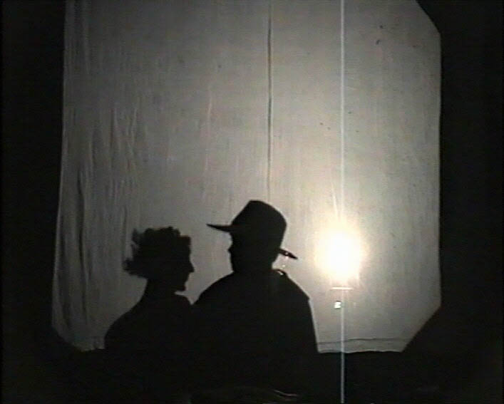Profile shadows of Agnes and Matilda in a secret meeting are projected on to a white screen.